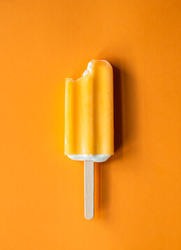 Orange ice cream creamsicle bar with a bite taken n orange background.
