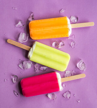 Three colorful popsicles with ice on a purple background