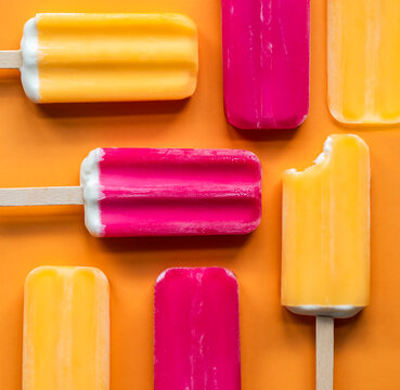 Colorful fruit ice popsicles on an orange background