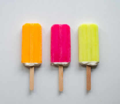 Three bright colorful popsicles in a row on white background.