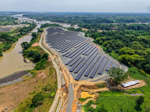 Aerial view of a large solar farm with rows of photovoltaic panels situated near a winding river and surrounded by lush tropical forest in Monrovia, Liberia.