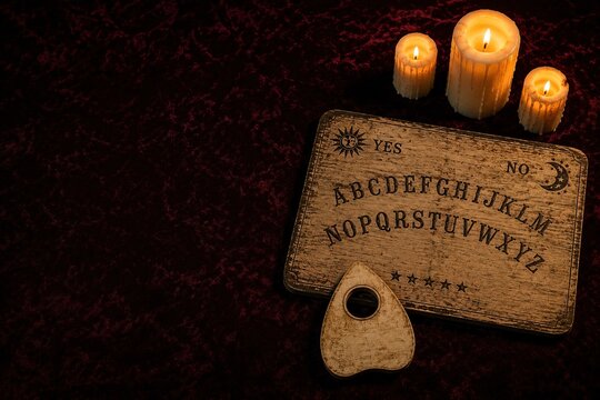 White spirit board with planchette and lit candles on dark red velvet