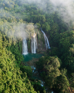 Aerial view of Cikaso Waterfall cascading into a turquoise pool surrounded by dense tropical rainforest and mist, West Java, Indonesia.