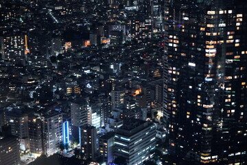 夜の都市景観、高層ビル群が灯りで輝く。密集した建物群と道路のライトが広がる夜景。 © BRUCE