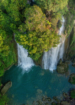 Aerial view of Cikaso Waterfall cascading into a turquoise pool surrounded by lush tropical vegetation and large mossy rocks in West Java, Indonesia.
