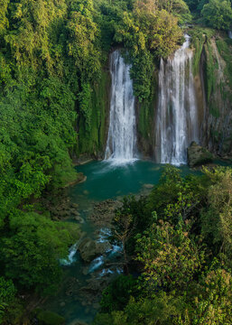 Aerial view of Cikaso Waterfall surrounded by dense tropical rainforest and lush green vegetation with turquoise water cascading into a rocky pool in West Java, Indonesia.