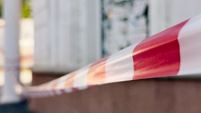 A red and white caution tape blocks the path in front of a blurry building. This tense barrier creates a feeling of worry and curious anxiety.