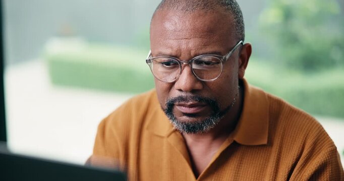 Man, glasses and laptop in home office with remote work, research and proofreading article for website. Mature, black person or freelance writer in house with computer, spectacles or review blog post