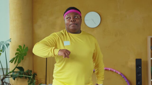 A man in a yellow shirt and pink headband dances with a hula hoop