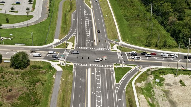 Aerial view of a modern road intersection with asphalt lanes, traffic lights, and vehicles driving through the junction in the United States.