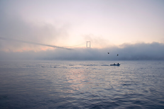 View of July 15 Martyrs Bridge (Bosphorus Bridge) with seagull and sunrise in fog clouds. Fishing boats in the foggy Bosphorus.