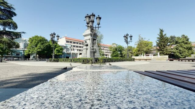 A historic monument stands tall in a sunny public square in Simferopol, Crimea. The serene and grand atmosphere brings a peaceful and nostalgic feeling to the beautiful city day.