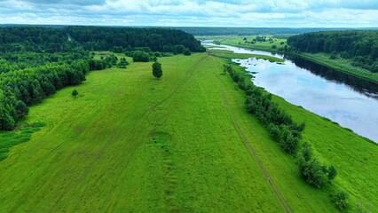 Obraz premium Vibrant lush green fields and winding river under cloudy skies in serene landscape view