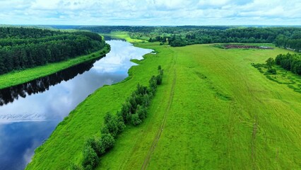 Obraz premium Aerial view of lush green fields bordering a calm river under a partly cloudy sky