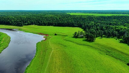 Obraz premium Aerial view of lush green fields and winding river under bright blue sky with scattered clouds