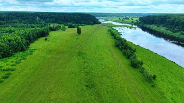 Vast green landscape featuring river banks, patches of trees, and cloudy sky in expansive view