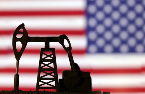 Texas, United States - May 7 2026: An oil pump jack is seen operating in front of a displayed U.S. flag, symbolizing domestic energy production and the petroleum industry in an American rural setting.