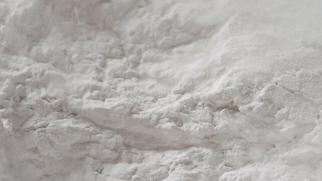 Ultra-detailed slow-motion macro shot of disrupted white powder surface being blown with strong air stream, breaking its structure and chipping it into small pieces | Corn starch cosmetic ingredient