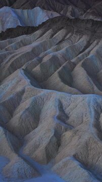 Vertical Screen: Death Valley National Park Zabriskie Point California featuring dramatic eroded mudstone badlands with deep ridges and gullies in cool blue twilight tones creating otherworldly.
