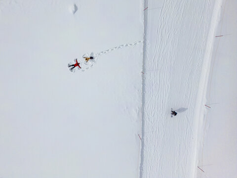 Aerial view of two people making snow angels in the snow near a snowboarder on a ski slope in Niseko, Hokkaido, Japan.