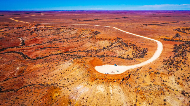 Aerial view of Deons Lookout featuring a gravel road winding through the arid red desert landscape of the outback in Birdsville, Queensland, Australia.