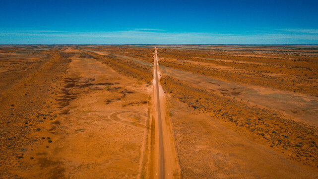 Aerial view of the long, straight road stretching through the arid red-earth landscape near Deons Lookout in Birdsville, Queensland, Australia.