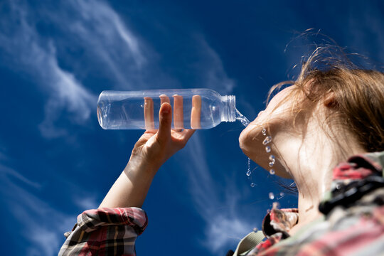 Low angle view of a female traveler quenching her thirst by drinking water flowing down her skin under a bright blue sky. Outdoor wellness and an active lifestyle.