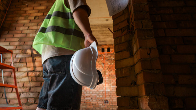 Construction worker holding hard hat at unfinished brick building site