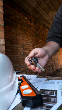Construction worker holding keys with safety helmet and level tool on blueprints