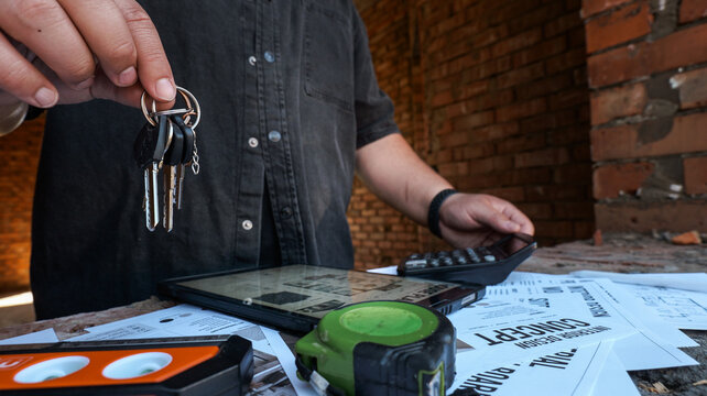 Construction worker holding keys with blueprints and tools on table