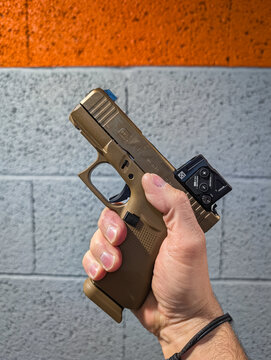 BALTIC STATES - JUNE 26, 2026: Close-up of a person holding a new model Glock 43X pistol in coyote brown color with a 15-round magazine and red dot sight at a shooting range.