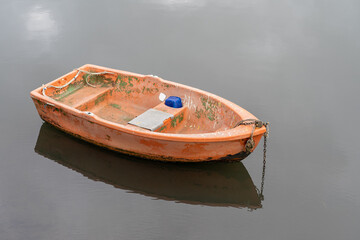 Small weathered orange dinghy floats on calm, grey water © Em Neems Photography