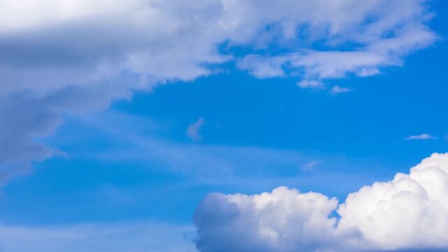 Slow pan of cumulus clouds drifting across bright blue daytime sky with layered white and gray cloud formations and soft sunlight
