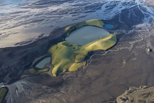 Aerial view of the Laki volcanic craters with moss-covered slopes and glacial meltwater pools surrounded by vast dark volcanic sand plains in Kirkjubaejarklaustur, Skaftarhreppur, Iceland.