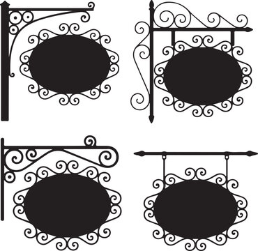 Wrought iron street signs set with ornate scrolls and oval boards for cafe or shop branding hanging on metal brackets and supports.
