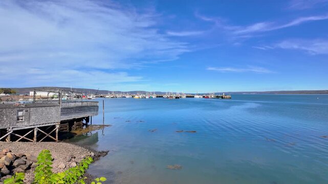Slow motion footage overlooking Digby Harbour and the Bay of Fundy in Digby Nova Scotia Canada featuring a working fishing port calm coastal waters wooden wharves moored boats and a dramatic blue sky
