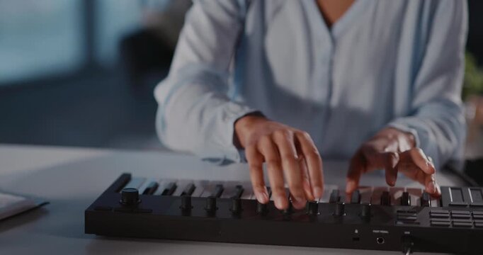Young african american woman sitting at table playing electronic piano synthesizer recording music tracks and singing song inside home. Hobby activity. Close-up.