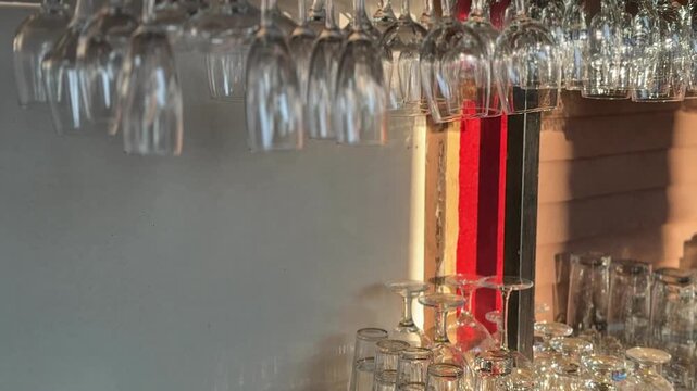 Rows of hanging wine glasses above a bar counter in warm ambient light. Hospitality, restaurant interior, bar service, dining, beverage culture and nightlife concept.