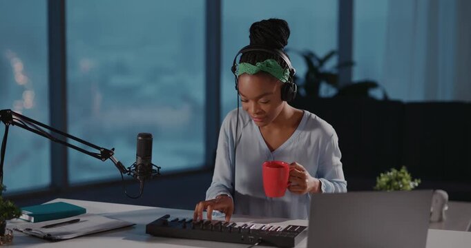 Pretty African American Talented Woman Musician Making Music at Home. Cheerful Esctatic Black Girl Playing Electronic Synthesizer Piano Keyboard in Headphones.
