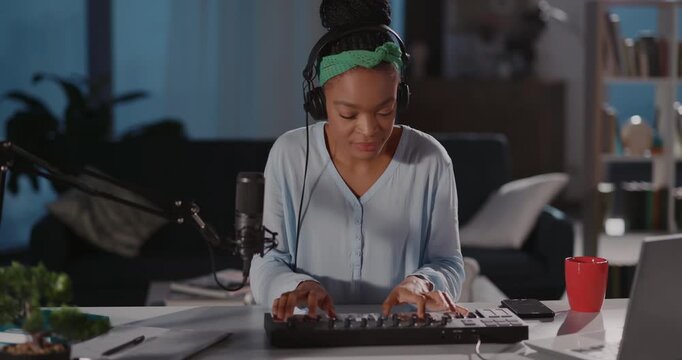 Delighted young attractive african female musician recording music listening in headphones and playing electronic keyboard piano synthesizer. Portraits.