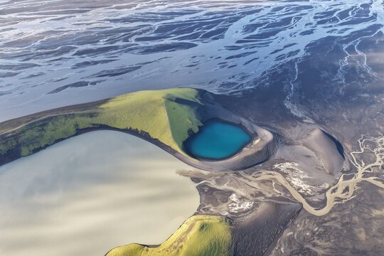 Aerial view of Laki volcanic crater with green mossy slopes and a turquoise lake, surrounded by dark volcanic sand and glacial river patterns in Kirkjubaejarklaustur, Skaftarhreppur, Iceland.