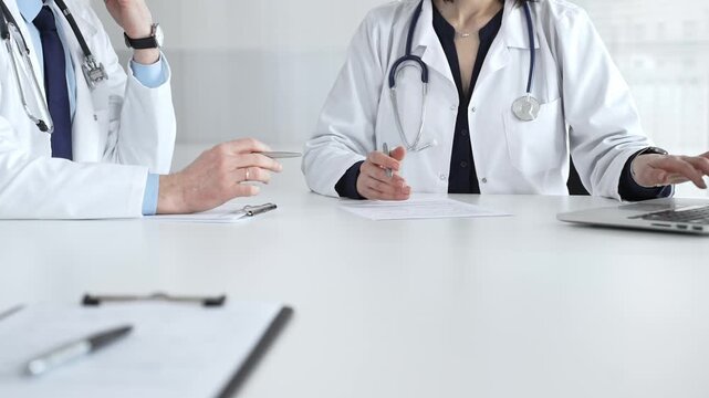 Medical professionals in lab coats writing notes during clinical consultation at modern healthcare office. Medical team meeting