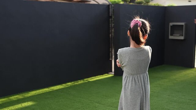 Little girl runs on green grass outdoors. She smiles, arms outstretched, joyful. Dark walls frame her playful movement. Bright sunlight highlights her happy expression