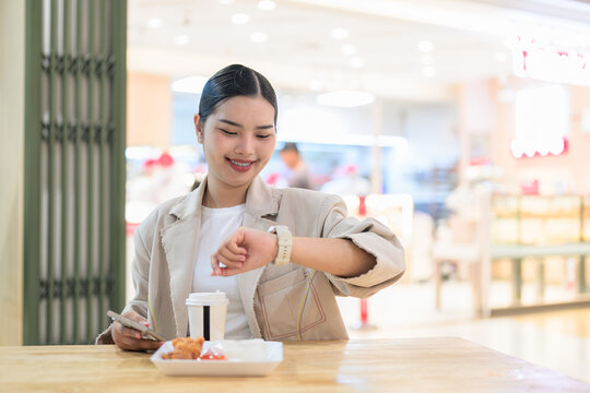 Smiling young Thai Isan businesswoman checking her smartwatch during lunch break