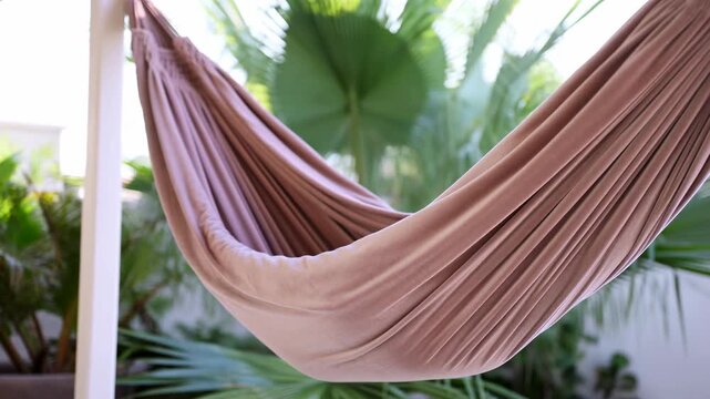 Mauve hammock in bright sunroom slowly stretches from relaxed drape into slightly taut pleats, revealing soft folds, curved support lines, indoor tropical light, and calm decorative atmosphere