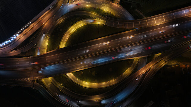 Aerial view of highway intersections at night with vibrant car light trails and traffic flow in Porto, Portugal.