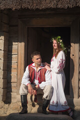 Fototapeta premium Romantic slavic couple in love wearing traditional embroidered clothes by wooden house with copy space
