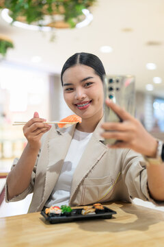 Smiling young Thai Isan businesswoman taking a selfie with sushi during lunch break