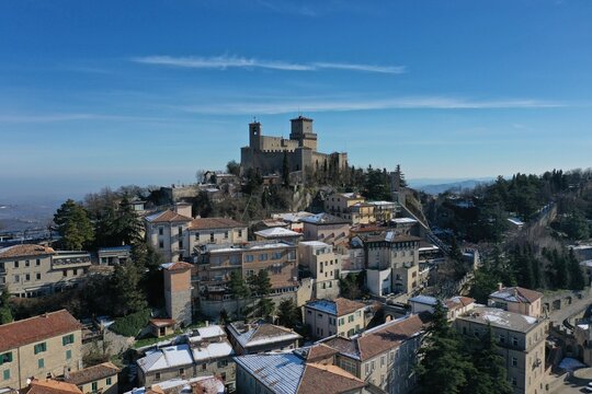 Aerial view of Guaita Tower, the historic fortress on Mount Titano, overlooking snow-dusted rooftops of the old town under a clear blue sky in San Marino, San Marino, San Marino.