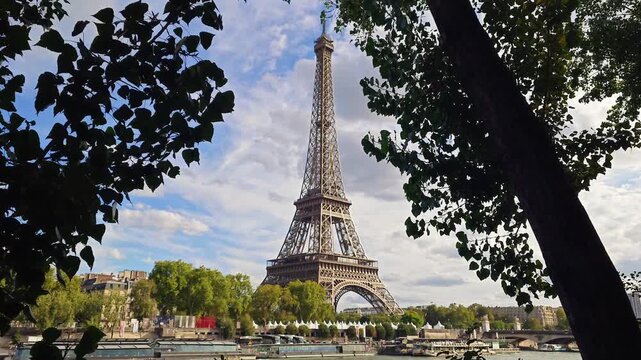 A scenic view of the Eiffel Tower framed by green tree leaves under a cloudy sky in the French capital